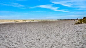A wide sandy beach with a clear blue sky and distant buildings. - Charming Gulf front condo w/ balcony full kitchen central AC and WD (Treasure Island)