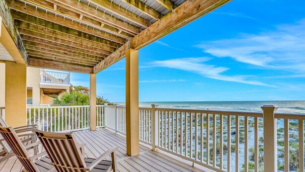 A wooden deck with chairs, a railing, and a view of the beach. - Charming Gulf front condo w/ balcony full kitchen central AC and WD (Treasure Island)