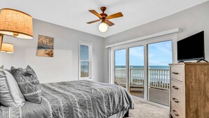 A bedroom with a bed, a ceiling fan, a TV, a dresser, and a sliding glass door leading to a balcony with a view of the beach. - Charming Gulf front condo w/ balcony full kitchen central AC and WD (Treasure Island)