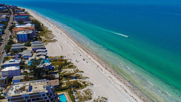 An aerial view of a coastal area with a beach, buildings, and a clear blue sky. - Spacious and family friendly with pool dock and just steps to the beaches (Indian Shores)