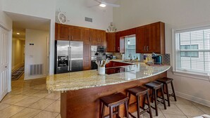 A modern kitchen with granite countertops, stainless steel appliances, wooden cabinets, and a central island with bar stools. - Spacious and family friendly with pool dock and just steps to the beaches (Indian Shores)