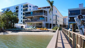 A waterfront hotel with multiple balconies, a wooden deck, and a kayak on the beach. - Spacious and family friendly with pool dock and just steps to the beaches (Indian Shores)