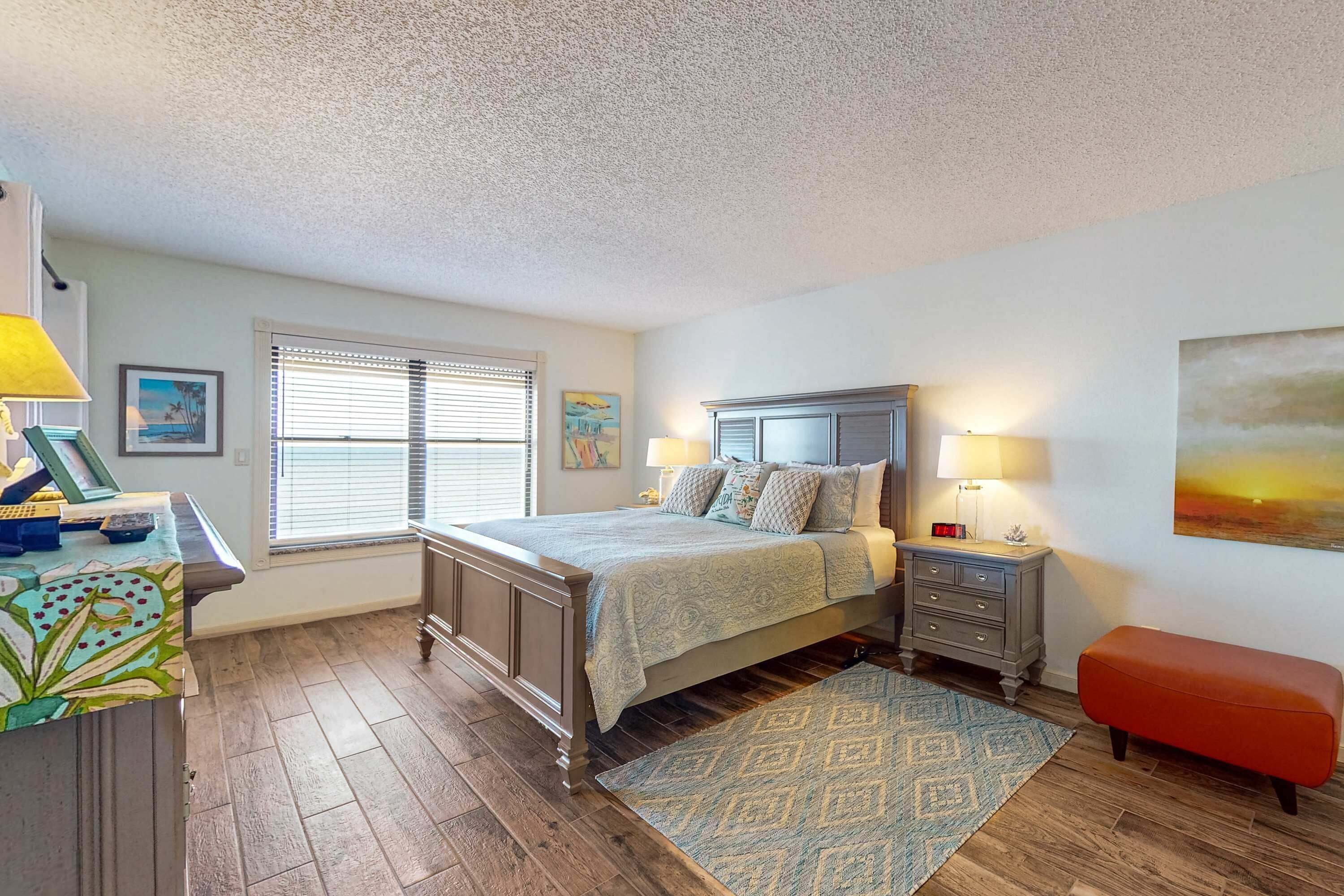 A bedroom with a bed, bedside tables, a desk, and a window with blinds.