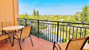 A balcony with two tables and chairs, offering a view of a residential area with trees and houses.