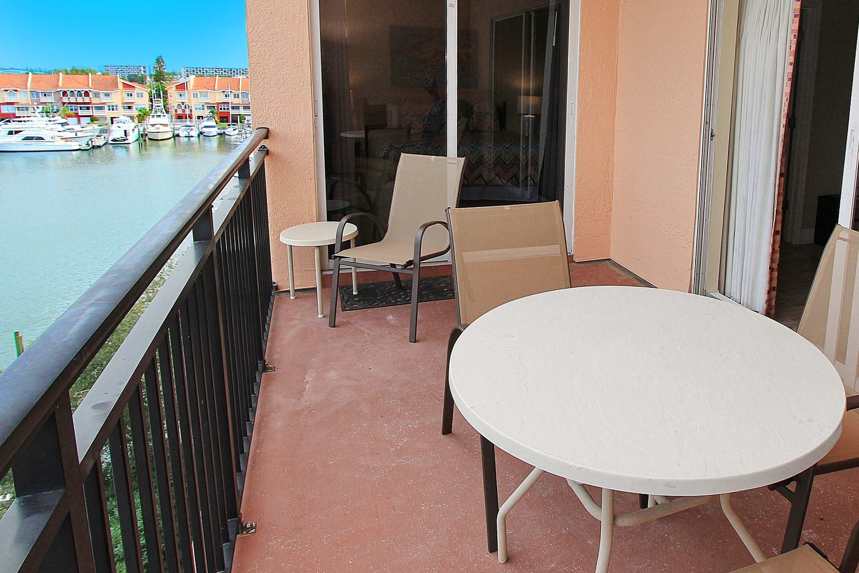 Un balcon avec une table blanche et deux chaises, donnant sur une marina où sont amarrés des bateaux.