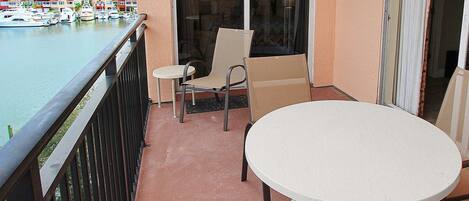 Un balcon avec une table blanche et deux chaises, donnant sur une marina où sont amarrés des bateaux.