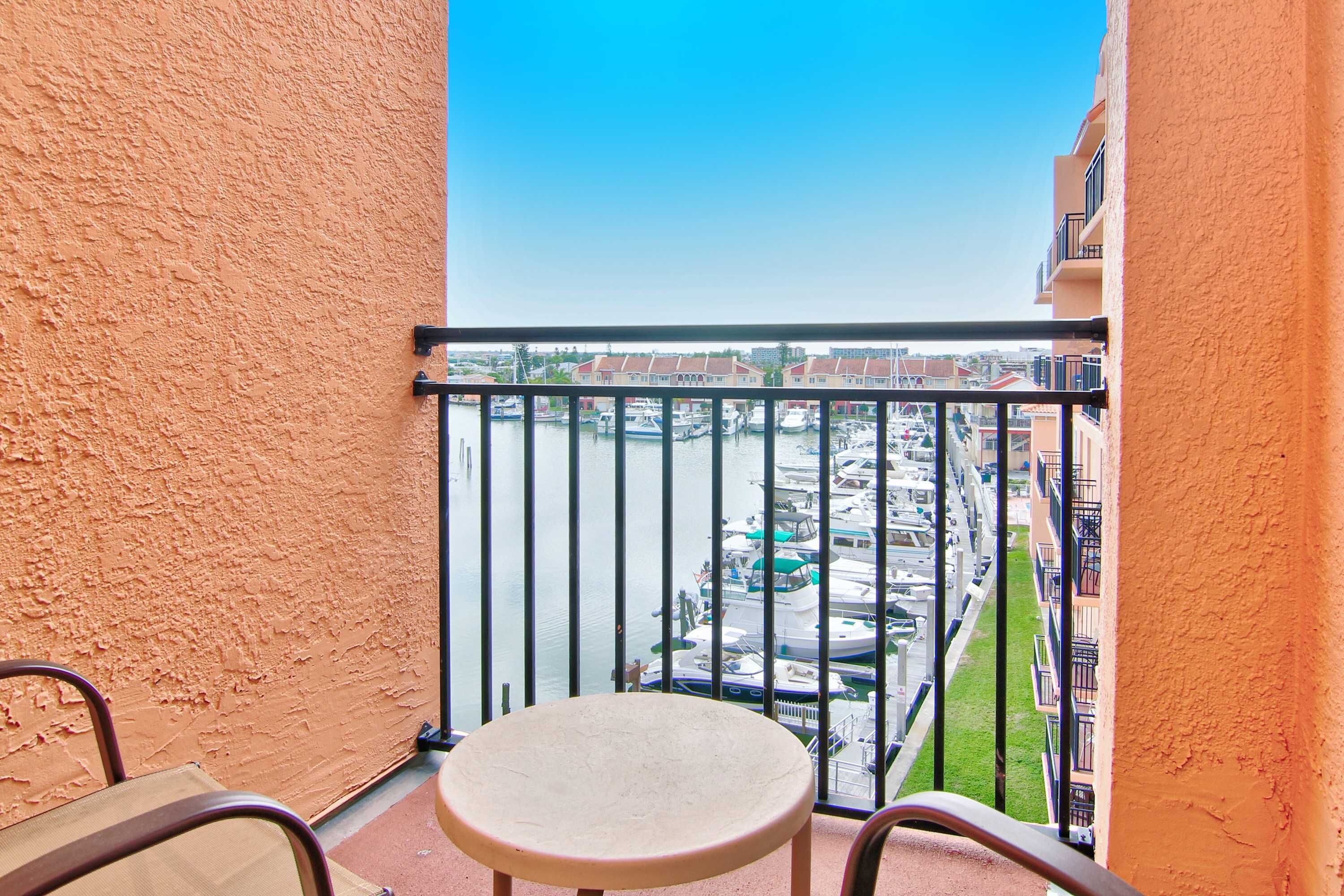 A balcony with a table and chairs, overlooking a marina with boats and buildings.