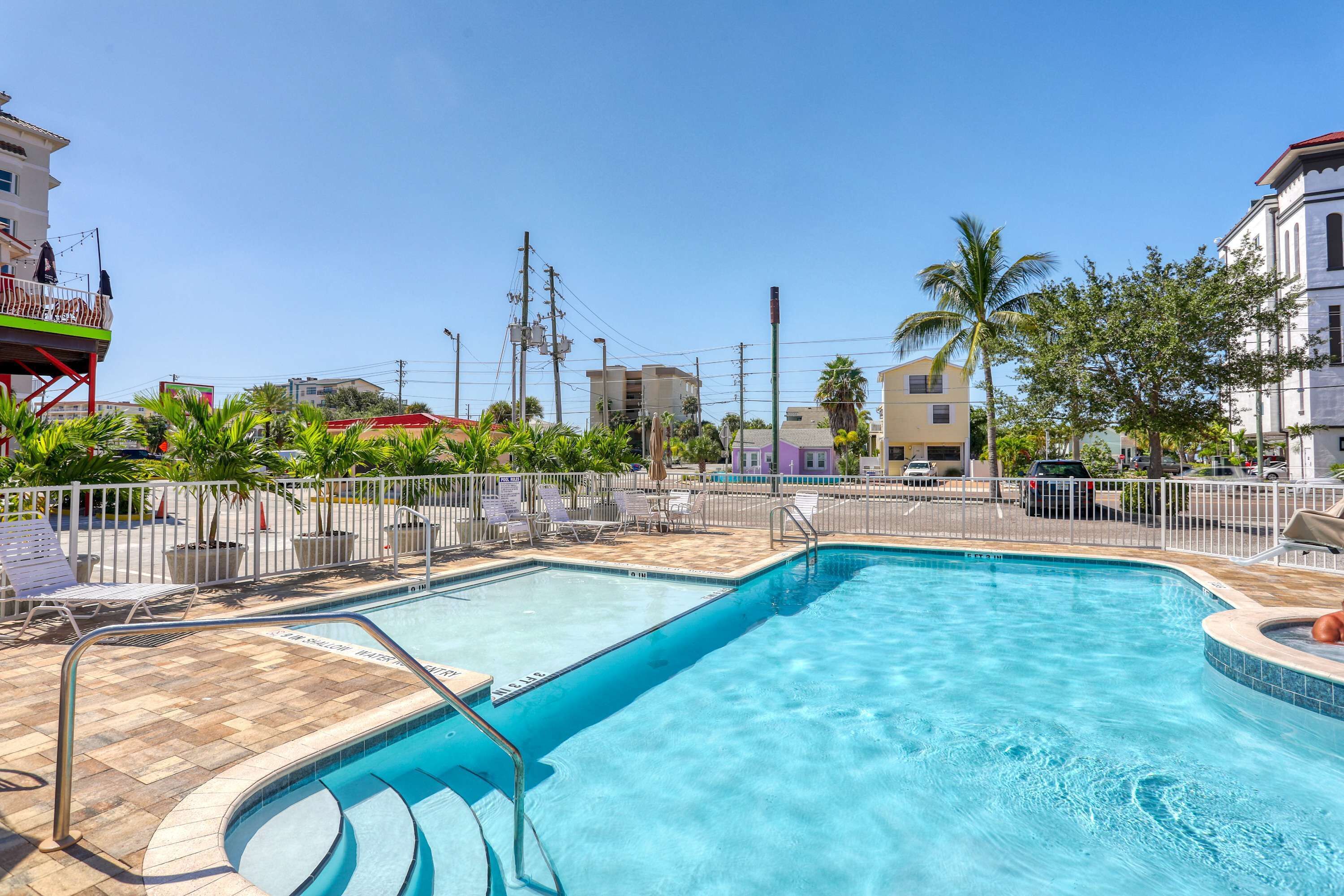 A rectangular swimming pool with a tiled deck, surrounded by a white fence and several lounge chairs.