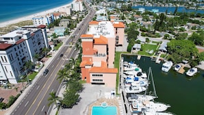 An aerial view of a coastal area with a marina, a swimming pool, and buildings with balconies overlooking the water.