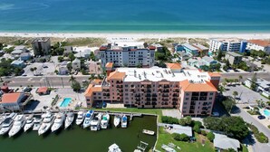 A marina with multiple boats docked, a large building with a red roof, and a beach in the background.