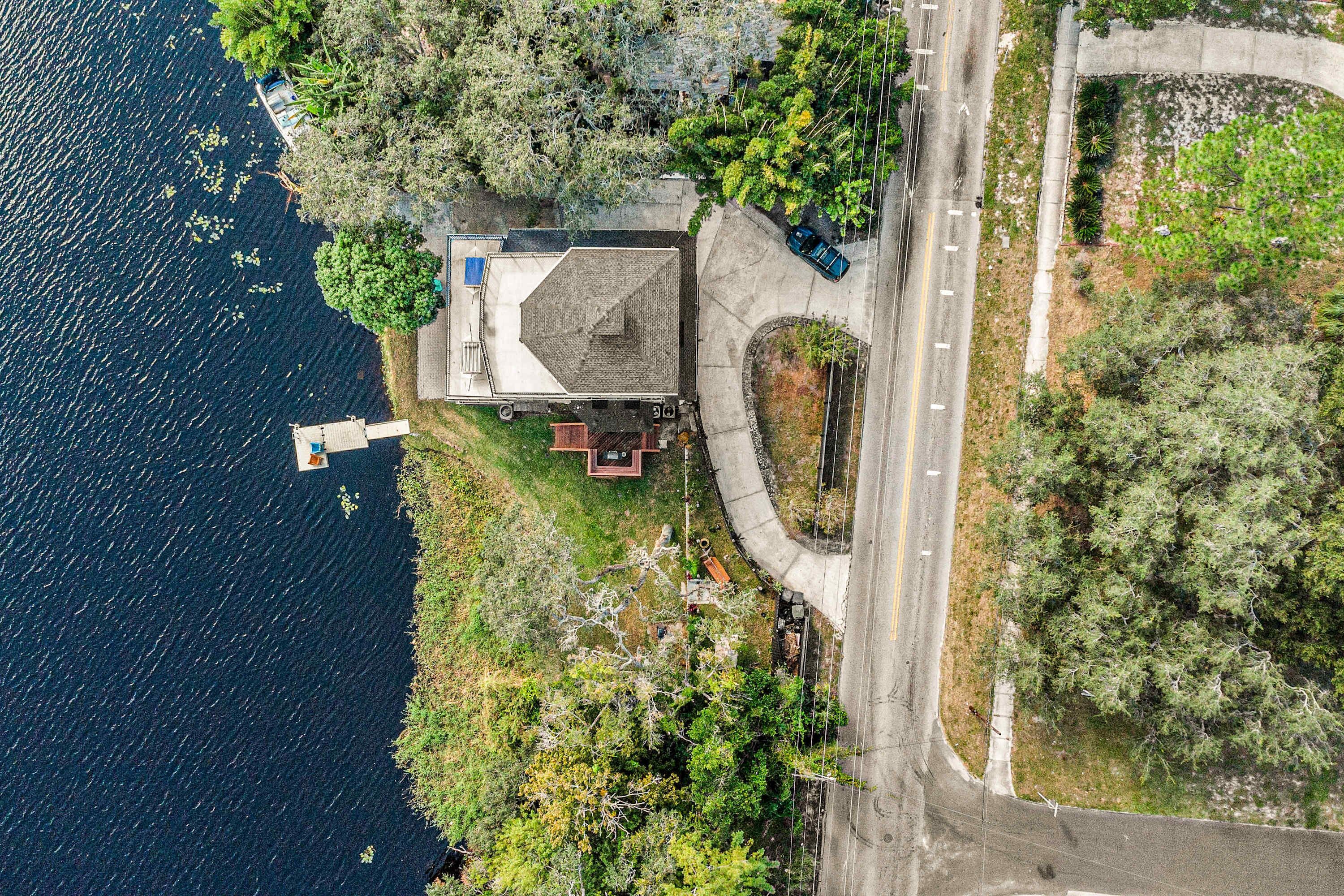 An aerial view of a house with a dock, surrounded by trees and a road.
