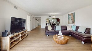 Un salon moderne doté d’un grand téléviseur à écran plat, d’un meuble de rangement en bois, d’un canapé d’angle en cuir et d’une table basse ronde.