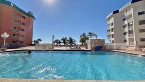 Une piscine, un ciel dégagé, des palmiers et un bâtiment doté de balcons.