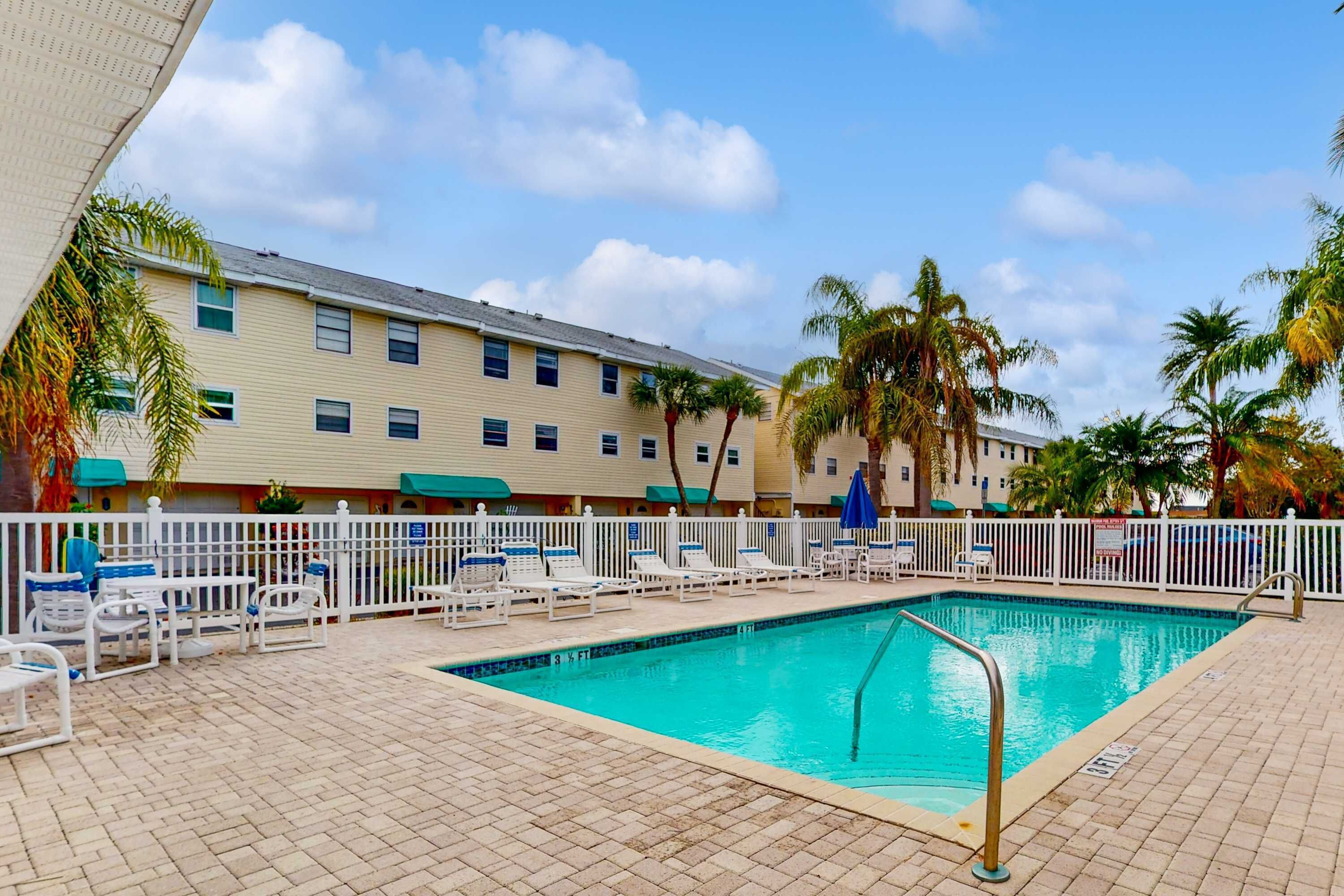 A swimming pool area with lounge chairs and a white fence.