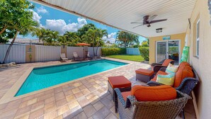 A covered outdoor swimming pool area with a patio, wicker furniture, and a view of the backyard. - Dog friendly home near beaches with private pool enclosed backyard grill WD (St. Pete Beach)