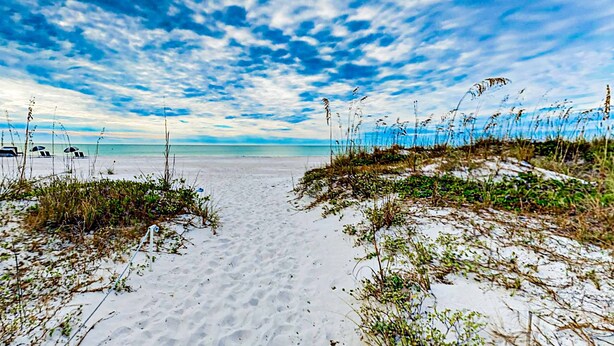 A beach with a clear path leading to the water, surrounded by sand and sparse vegetation. - Dog friendly home near beaches with private pool enclosed backyard grill WD (St. Pete Beach)
