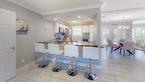 A modern kitchen with a central island, bar stools, and a dining area with chairs. - Dog friendly home near beaches with private pool enclosed backyard grill WD (St. Pete Beach)