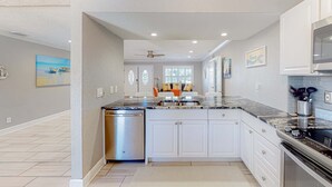 A modern kitchen with white cabinetry, a granite countertop, and a built-in dishwasher. - Dog friendly home near beaches with private pool enclosed backyard grill WD (St. Pete Beach)