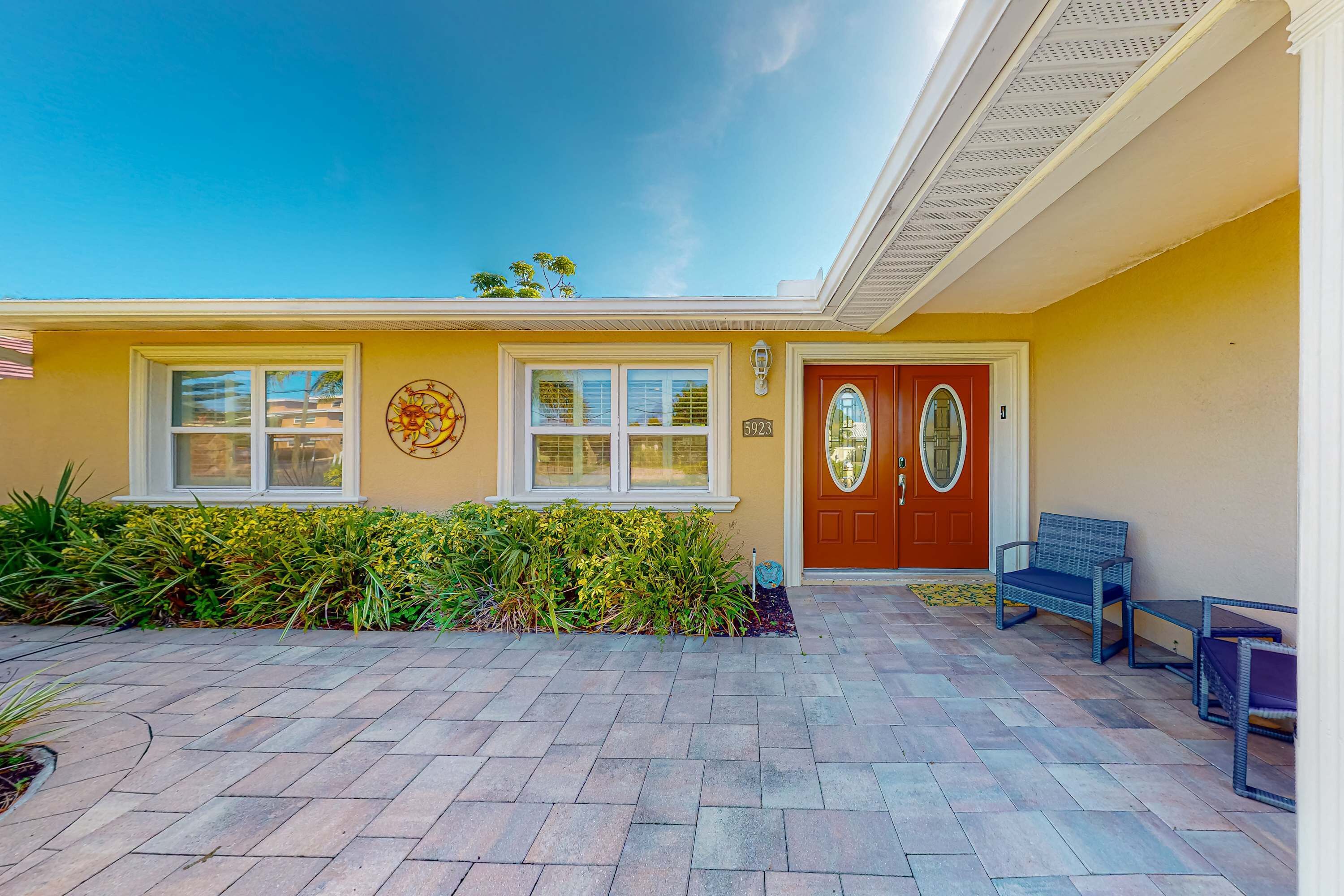 A yellow building with a red door, a number 5923, and a blue bench outside.