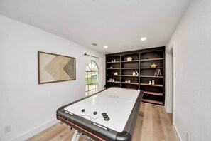 A pool table in a room with a large window, a bookshelf, and a framed picture on the wall.