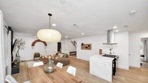 Un'ampia zona giorno con tavolo da pranzo in legno, una grande lampada a sospensione e una cucina con piano di lavoro in marmo.