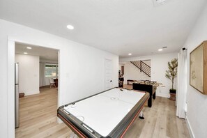 A modern living room with a foosball table, a dining area, and a staircase leading to another level.