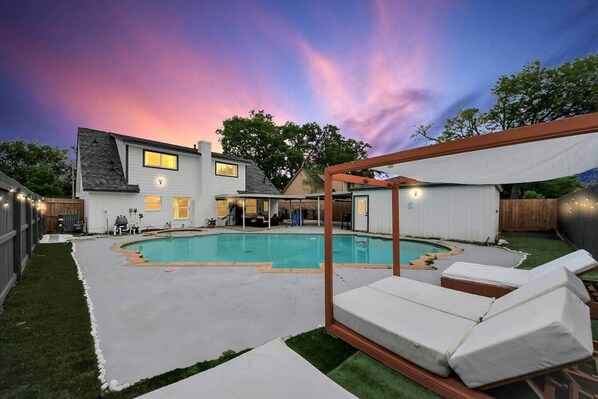 A backyard with a swimming pool, a covered patio, and a fenced area.