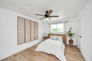 A bedroom with a bed, a ceiling fan, a window, a shoji screen, and a potted plant.