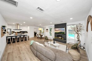 A modern living room with a fireplace, a dining area, and a kitchen.