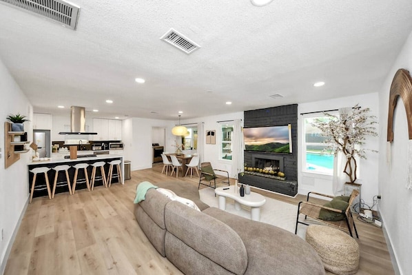 A modern living room with a fireplace, a dining area, and a kitchen. - *Pool | Modern Escape with Chic Vibes (Stafford)