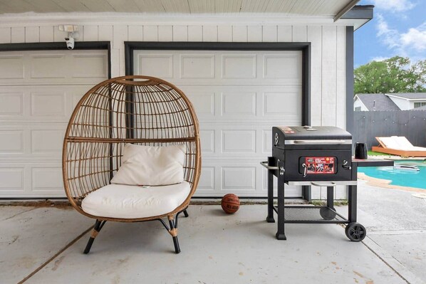 A wicker chair with a cushion, a barbecue grill, and a basketball on a concrete patio.