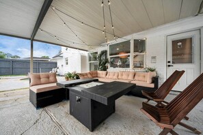An outdoor patio with a sectional sofa, a coffee table, and a wooden chair. - *Pool | Modern Escape with Chic Vibes (Stafford)