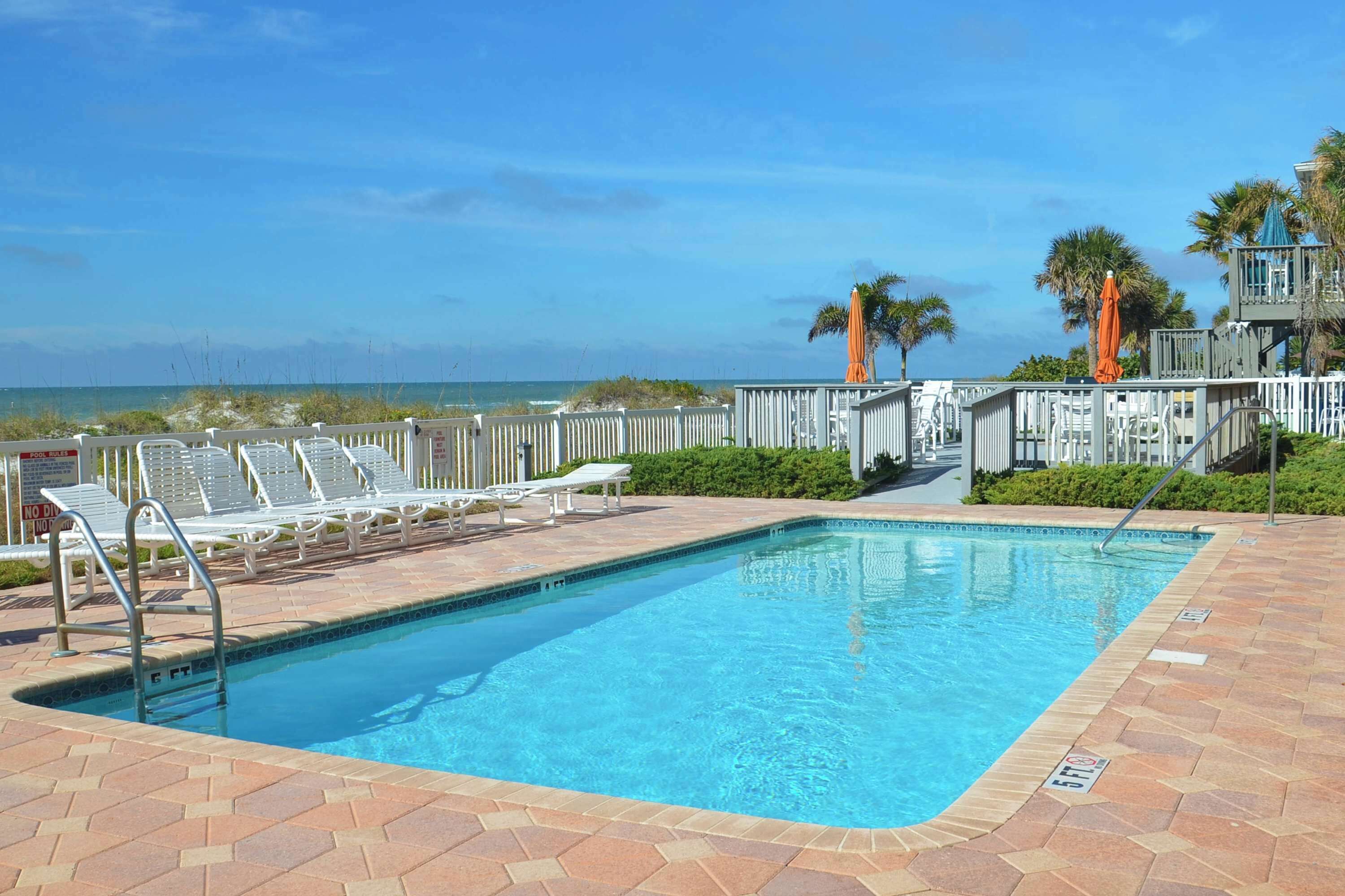 A swimming pool with a view of the ocean, surrounded by lounge chairs and a wooden deck.