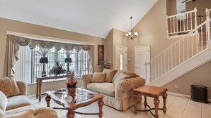 A living room with a beige sofa, a glass coffee table, and a wooden side table. There is a staircase with a white railing leading to an upper level. - Snowbird friendly elegant home with waterfront location pool grill fireplace (Largo)