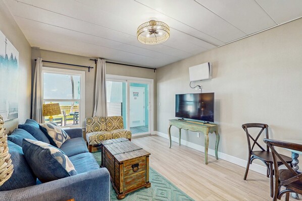 A living room with a sofa, armchair, wooden coffee table, television, and a dining table with chairs. - Beachfront condo on ground floor with full kitchen and central AC (Indian Shores)