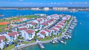 Uma marina com fileiras de edifícios brancos com telhados vermelhos, um campo de esportes e um céu azul límpido.