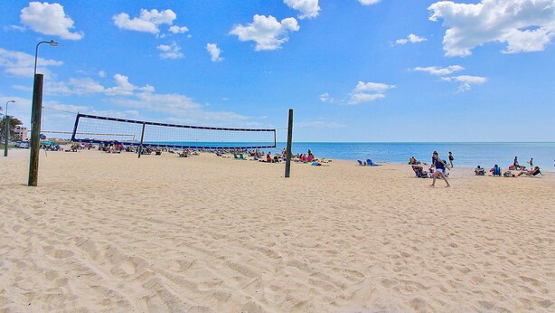 Uma quadra de voleibol de praia com rede, rodeada por areia e pessoas.