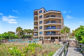 A multi-story hotel with balconies, a swimming pool, and a wooden boardwalk.