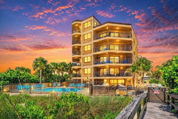 A multi-story hotel with balconies, a swimming pool, and a private entrance gate.
