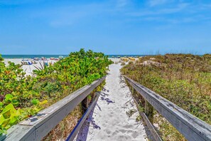 A sandy beach path leading to the ocean, surrounded by greenery and wooden railings.