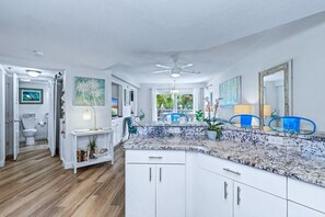 A modern kitchen with white cabinetry, a marble countertop, and a ceiling fan.