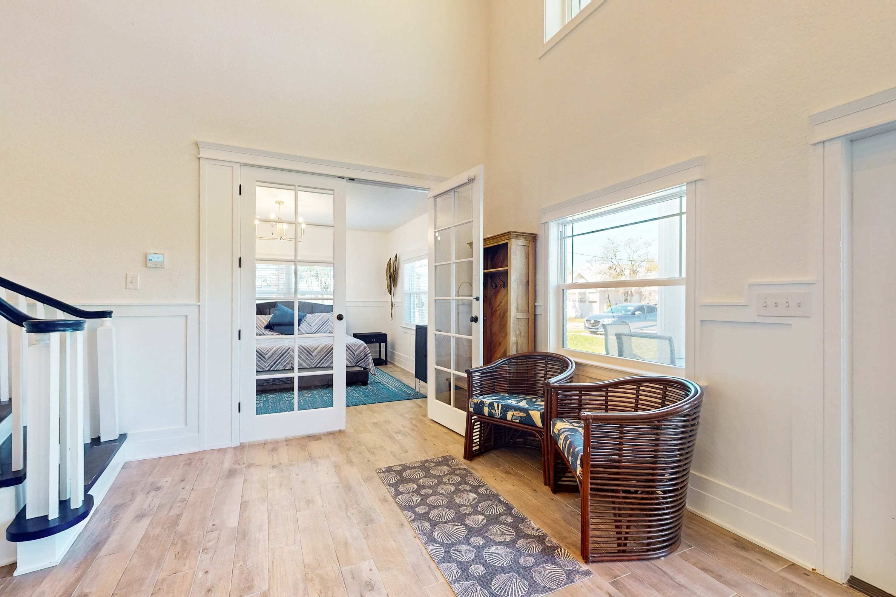 A spacious hallway with a wooden floor, a staircase, and a seating area with wicker chairs.