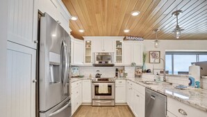 Une cuisine moderne avec des meubles blancs, des appareils en acier inoxydable et un plafond en bois.