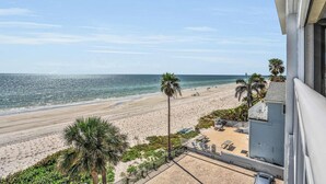 Une vue sur la plage, avec un balcon donnant sur l’océan, des palmiers et un immeuble doté d’un balcon.