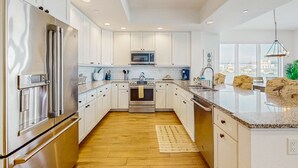 A modern kitchen with white cabinets, stainless steel appliances, a granite countertop, and a view of the city through large windows. - Waterfront Condo w WiFi Washer Dryer and Central AC Snowbird Friendly (Clearwater Beach)