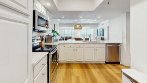 A modern kitchen with white cabinetry, stainless steel appliances, and a wooden floor. - Dreamy condo with panoramic Gulf vIews and beachfront heated pool and spa (Indian Shores)