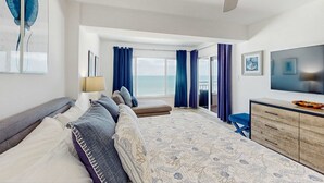 Ein modernes Hotelzimmer mit einem großen Bett, einem Fernseher, einer Holzkommode und einem Balkon mit Vorhängen.