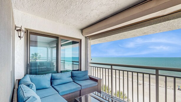 Ein Balkon mit blauer Couch und Glastüren, mit Blick auf einen Strand.