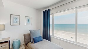 Ein Schlafzimmer mit Bett, einem Fenster mit Blick auf den Strand und zwei gerahmten Bildern an der Wand.