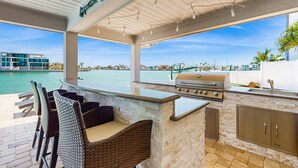 Een terras met een bar, rieten stoelen, een barbecue en uitzicht op het water.